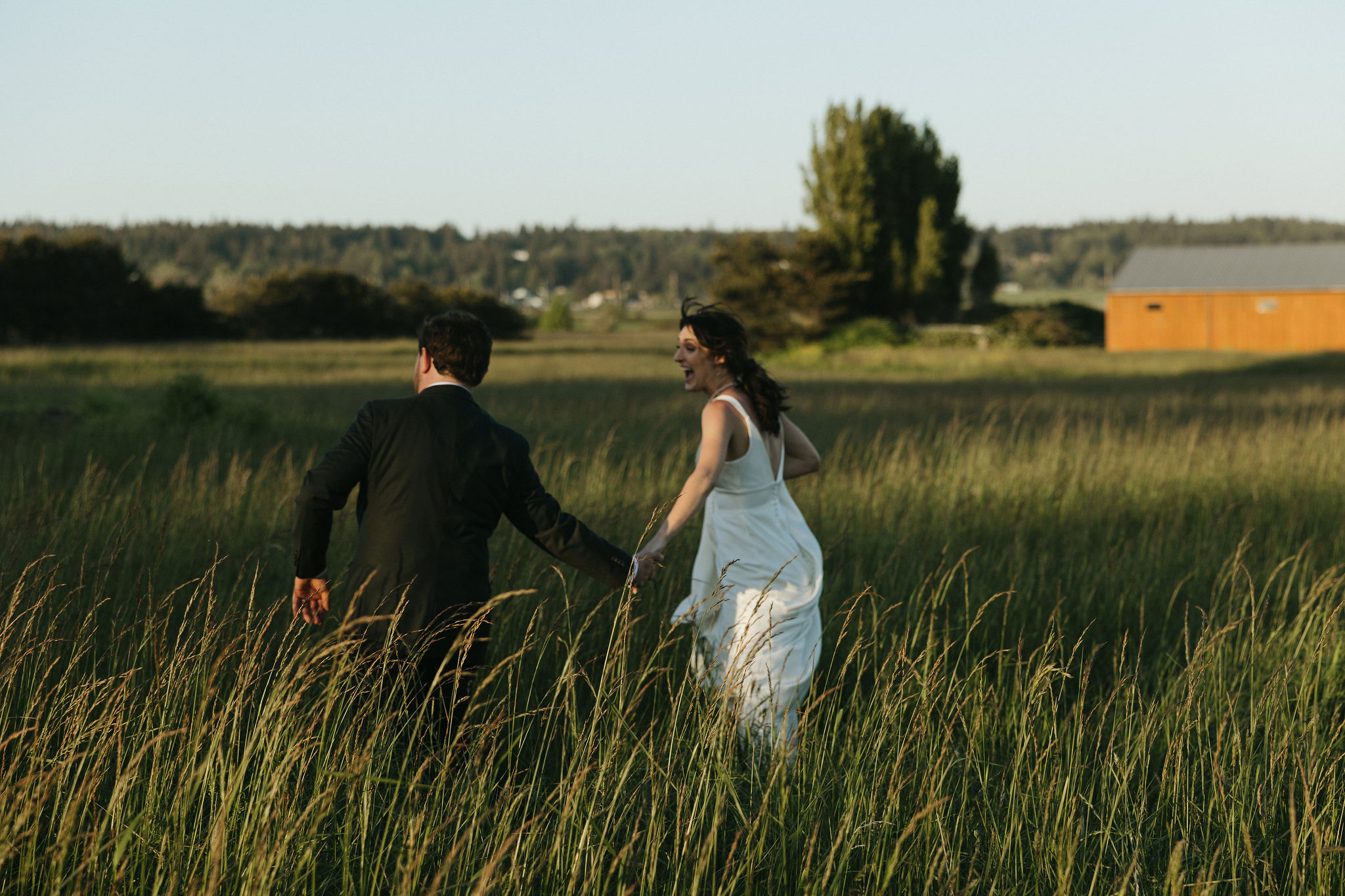 Bride and groom holding hands running in a grass field at Whidbey Island wedding venue