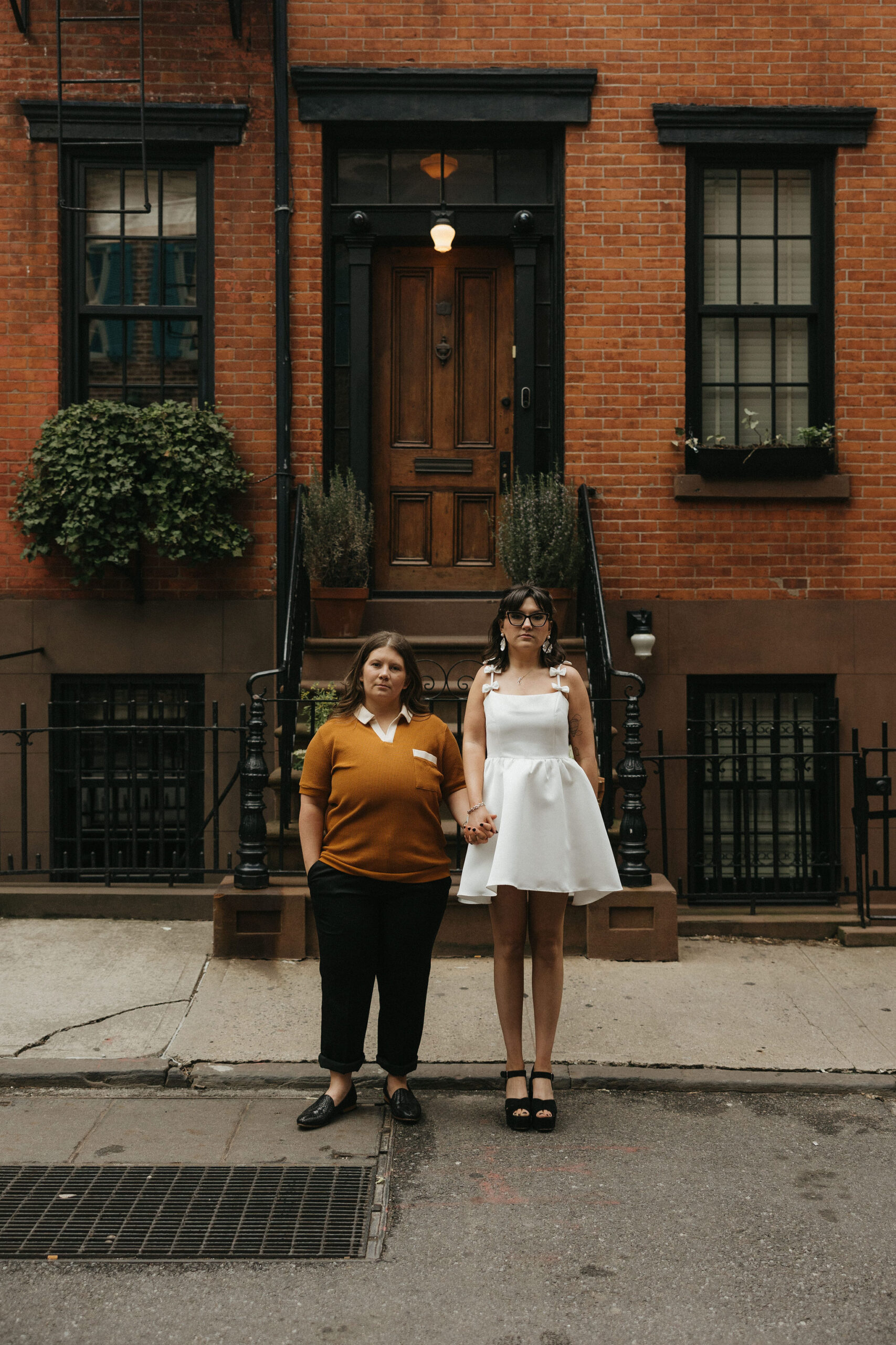 Newly engaged couple holding hands posing in front of a brick building on Cornelia Street