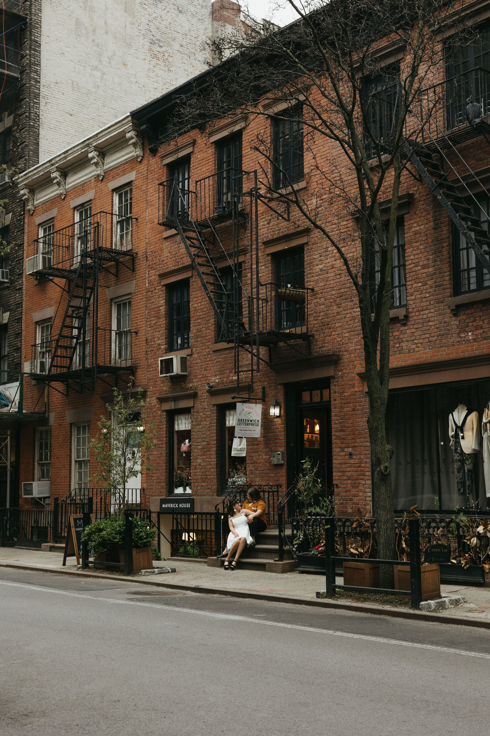 Newly engaged couple sitting in front of a brick house on Cornelia Street in New York