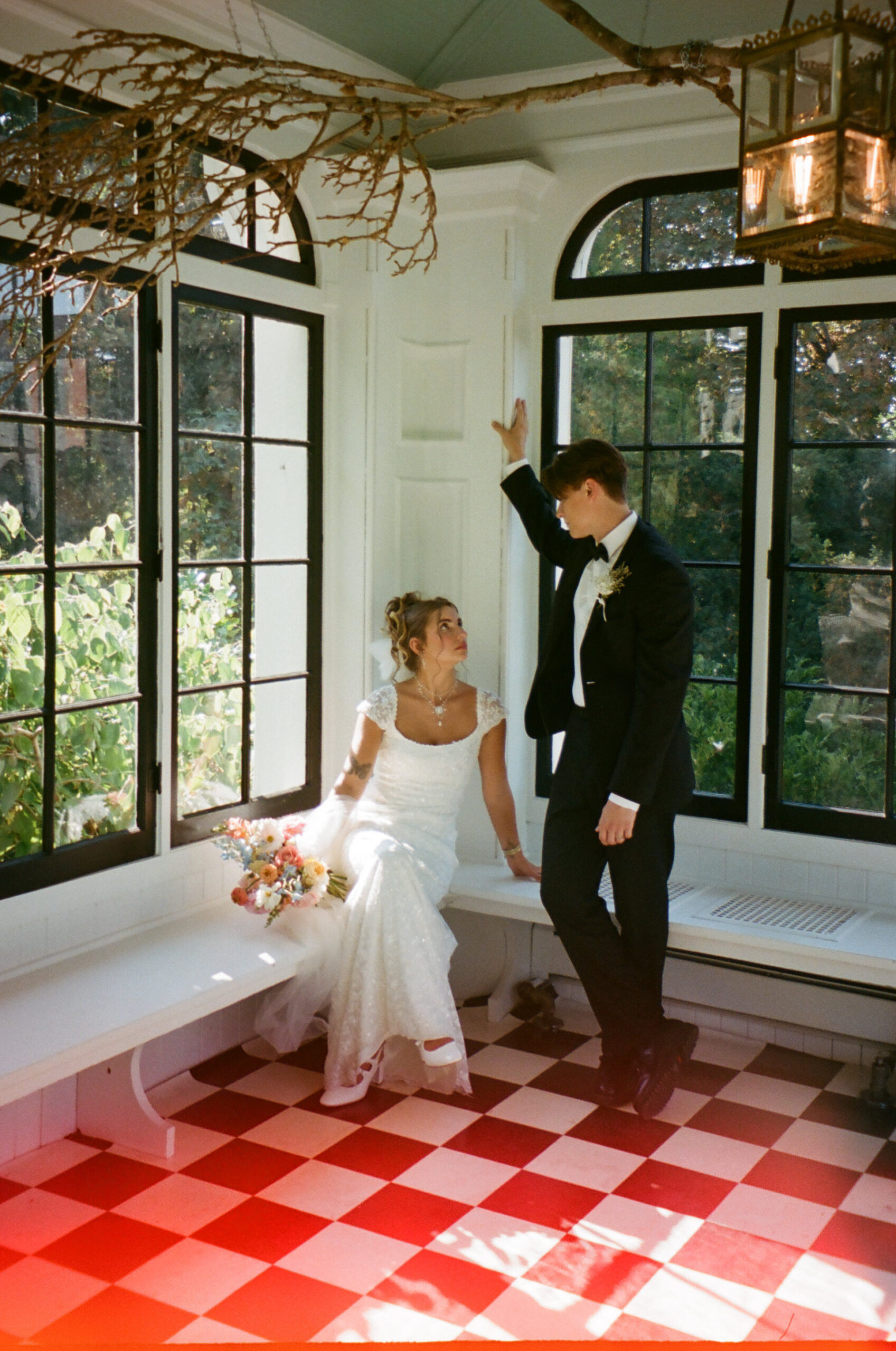 Film wedding photo of bride and groom standing in a room with checkered flooring looking at each other endearingly