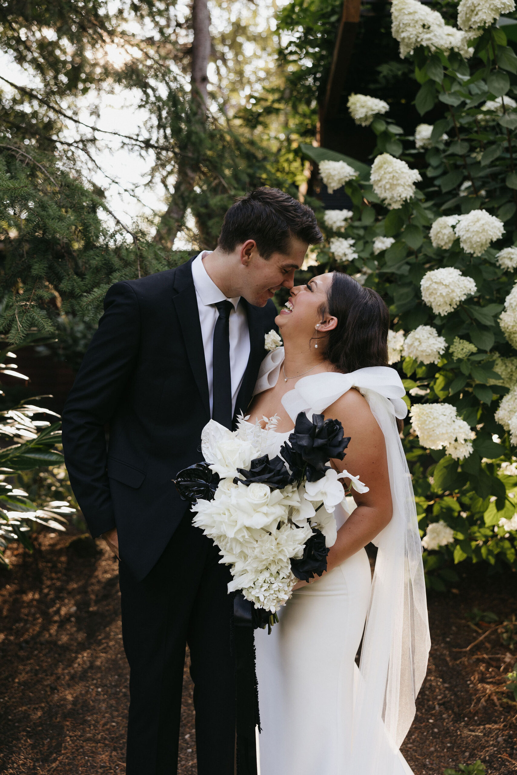 Bride and groom laughing smiling at one another posing in front of a rose bush 