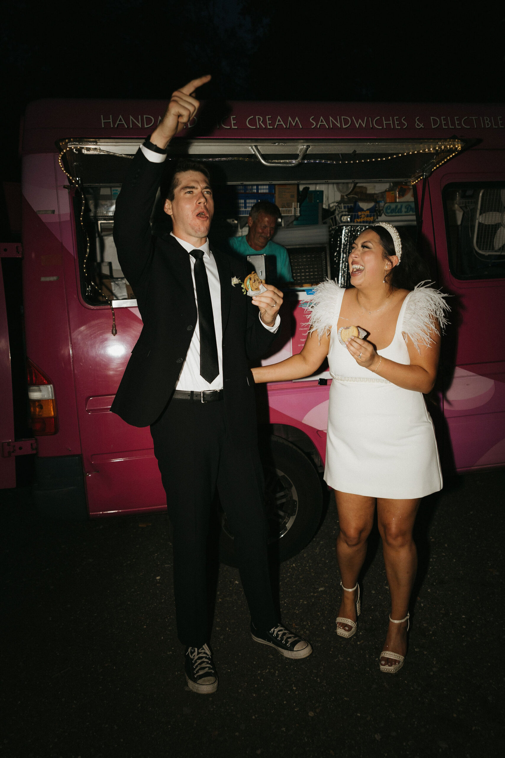 Bride and groom eating ice cream sand which cheering in front of a food truck 