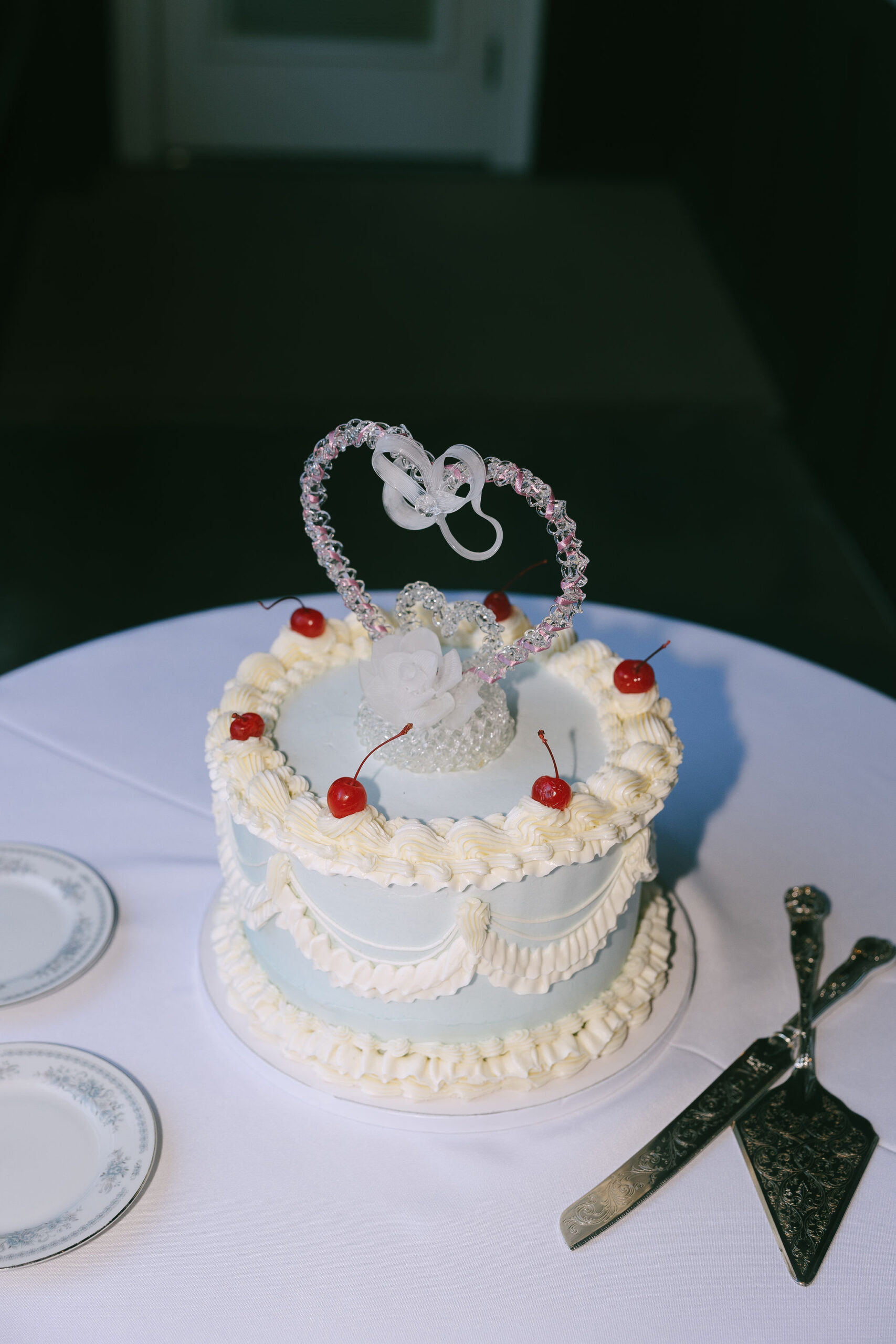 White and blue wedding cake with cherries and a heart shaped cake topper