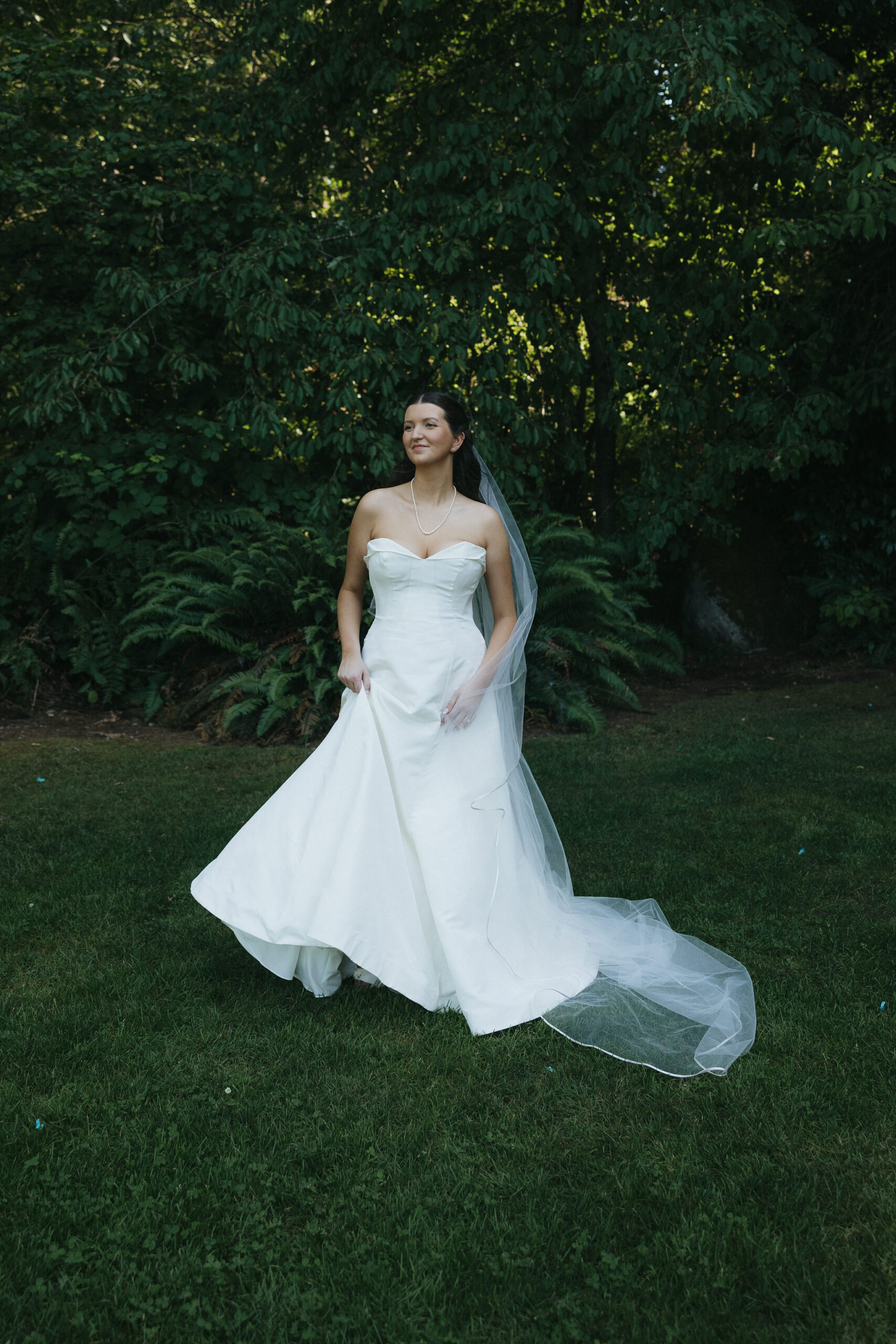 Bride in a white strapless A line wedding dress standing in a field of grass at the Robinswood House