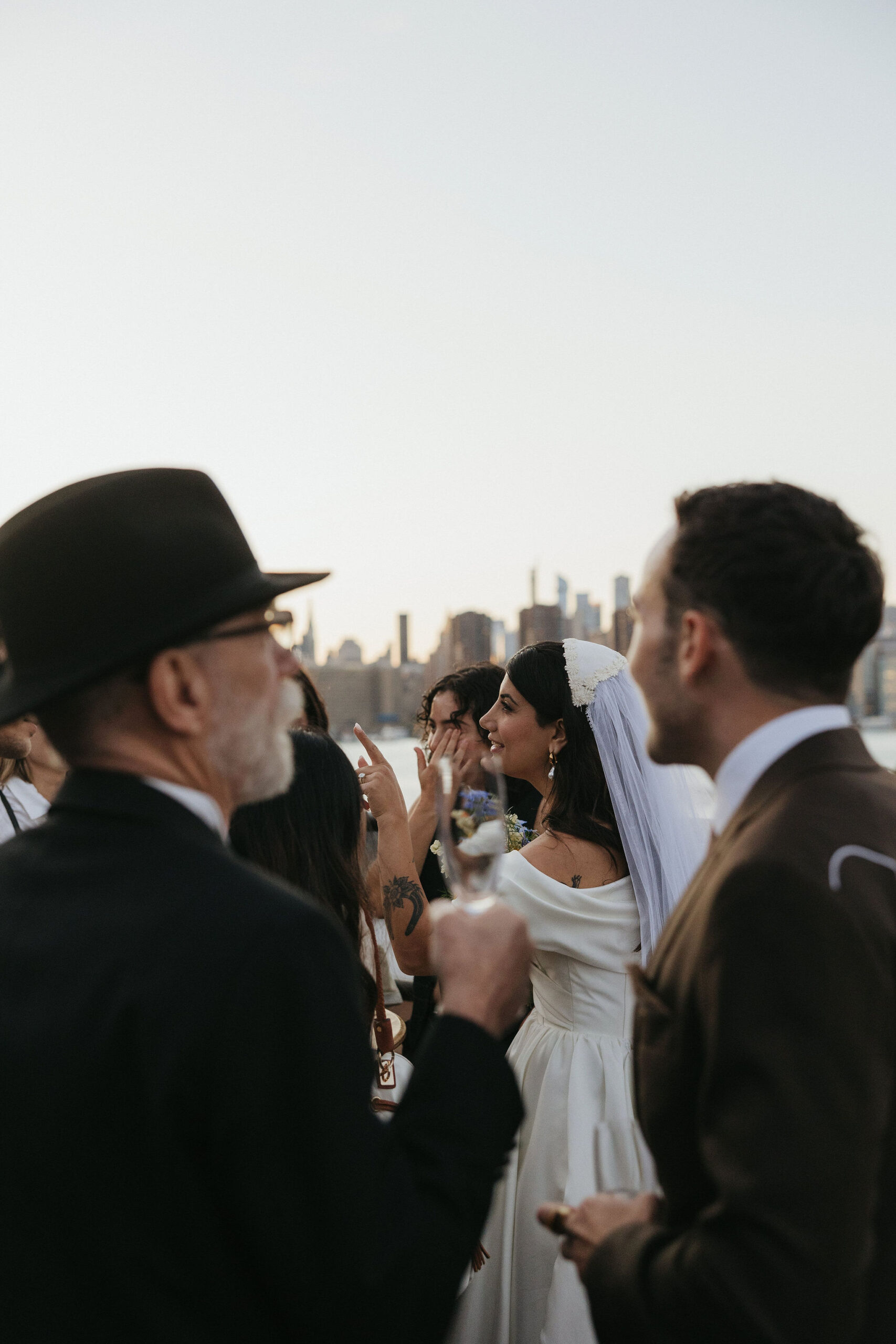 Greenpoint Loft Wedding reception rooftop gathering with guests laughing, the bride holding a bright bouquet of flowers.
