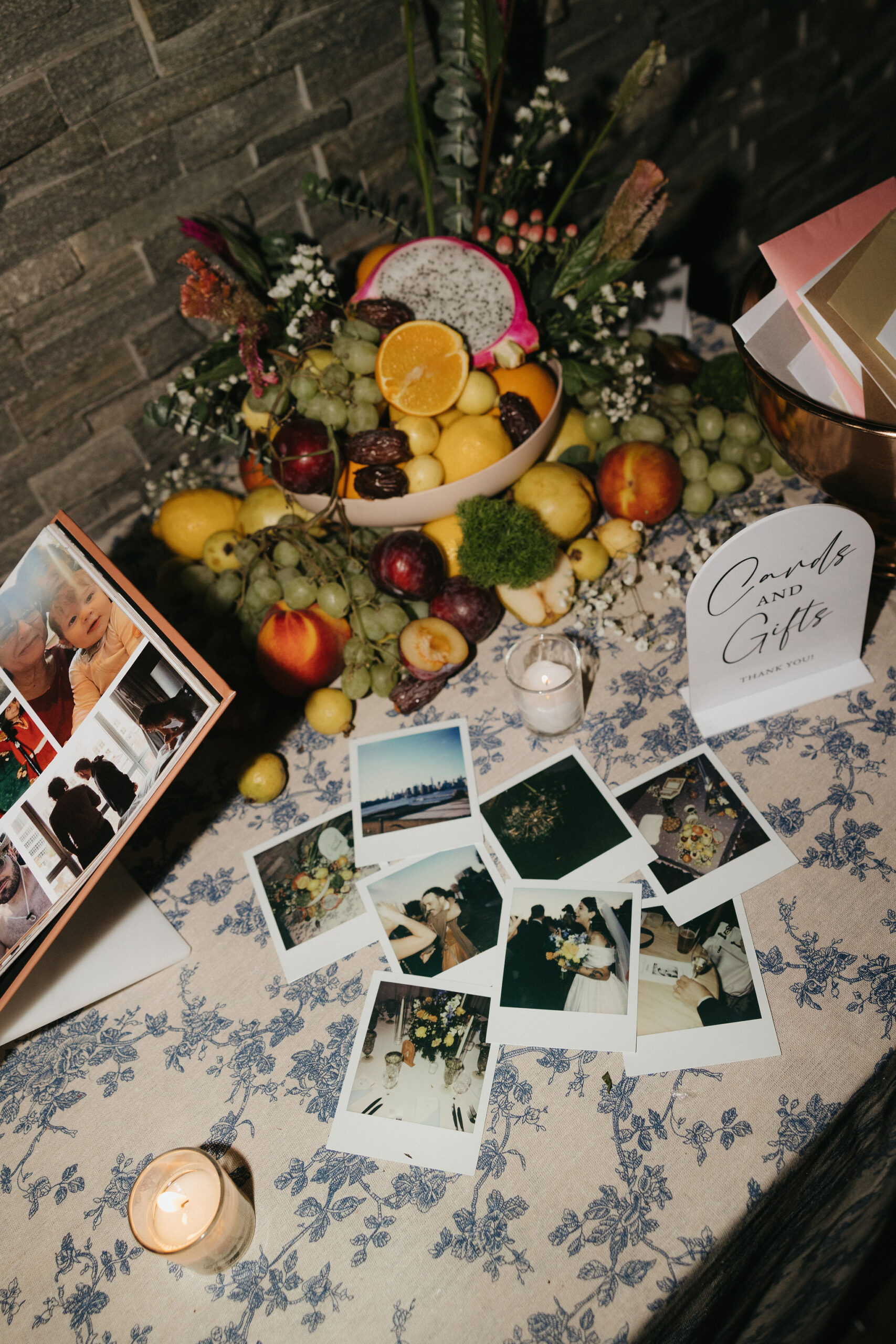 A display of fruit and Polaroid pictures scattered on a floral tablecloth at a Greenpoint Loft Wedding, showcasing intimate wedding memories.