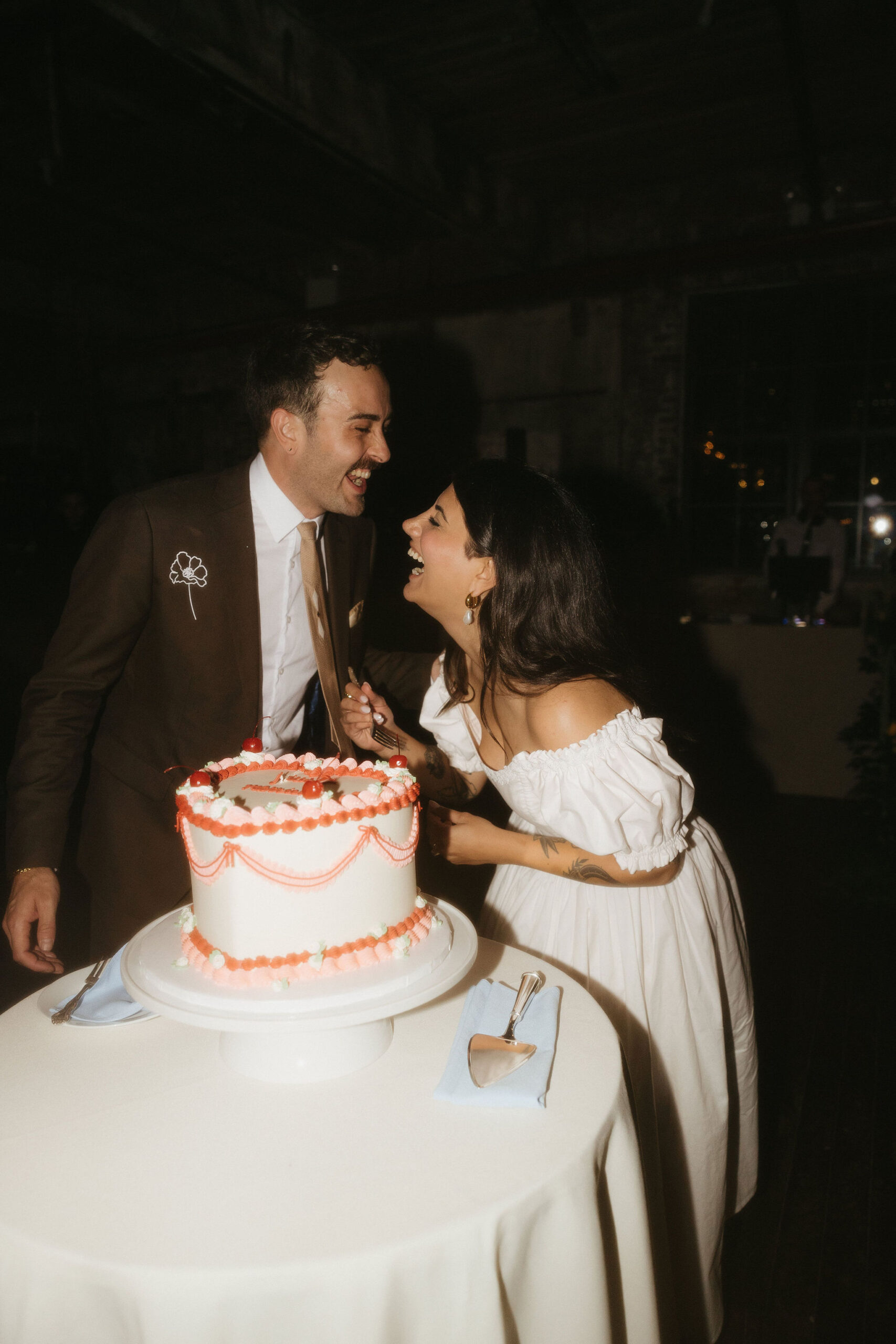 The bride and groom laughing and cutting their heart-shaped cake together at a Greenpoint Loft Wedding, sharing a candid and joyful moment. 