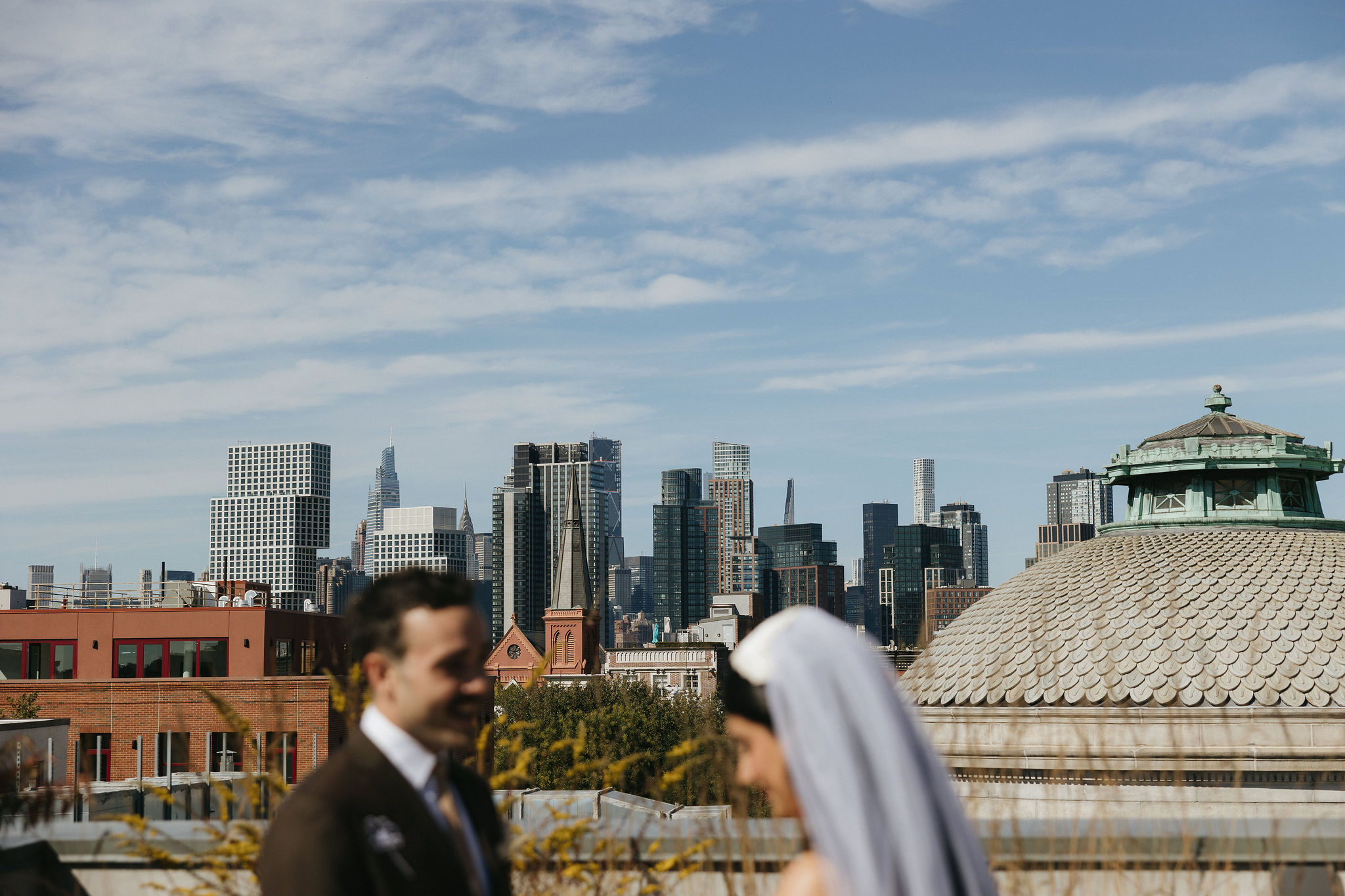 A wide shot of the skyline in a film wedding photo, with the couple slightly out of focus, highlighting New York’s cityscape.
