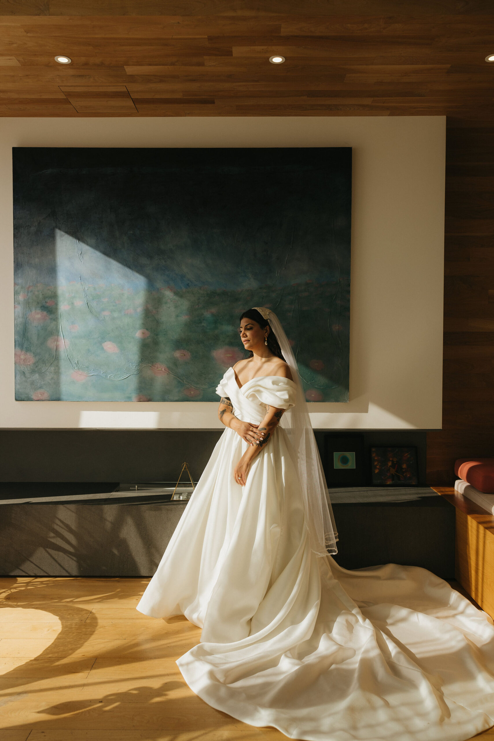 Bride standing in soft sunlight inside a modern room, her gown illuminated perfectly.